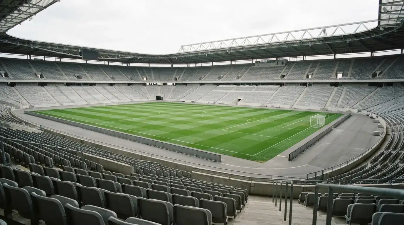 Ein leeres Fußballstadion bei Tageslicht von der Tribüne aus gesehen, der Rasen zeigt gleichmäßige Mähstreifen.